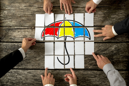 Top view of eight male hands assembling a colourful umbrella with cards over textured rustic desk